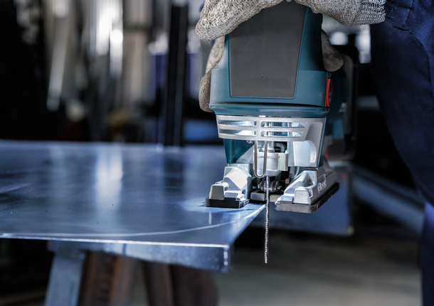 บุคคลที่สวมอุปกรณ์ความปลอดภัยใช้จิ๊กซอว์ตัดแผ่นโลหะ