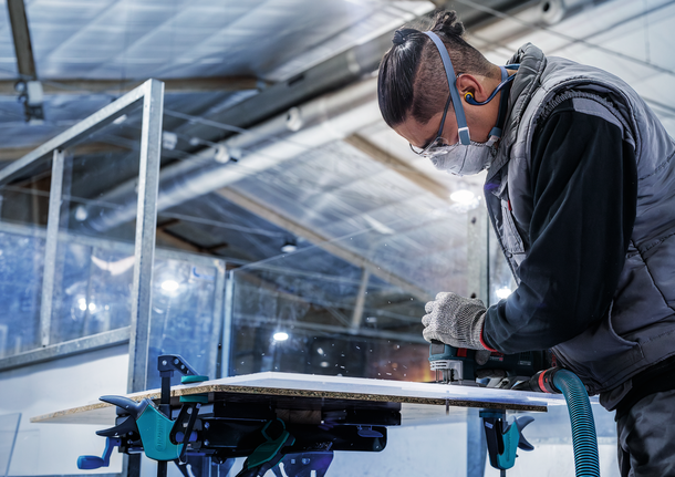 บุคคลที่สวมอุปกรณ์ความปลอดภัยกำลังตัดแผงไม้ด้วยเครื่องมือไฟฟ้า