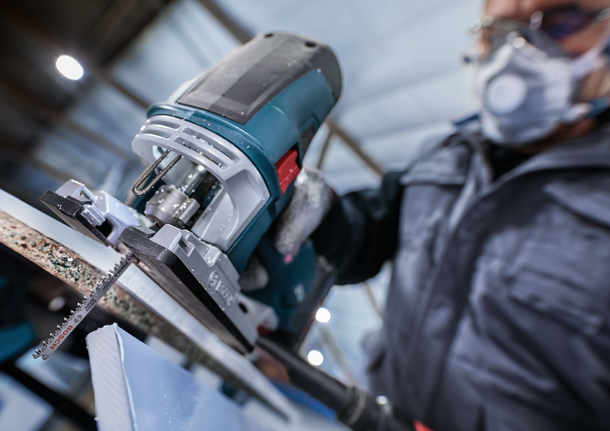 บุคคลที่สวมอุปกรณ์ความปลอดภัยใช้จิ๊กซอว์ตัดชิ้นวัสดุ