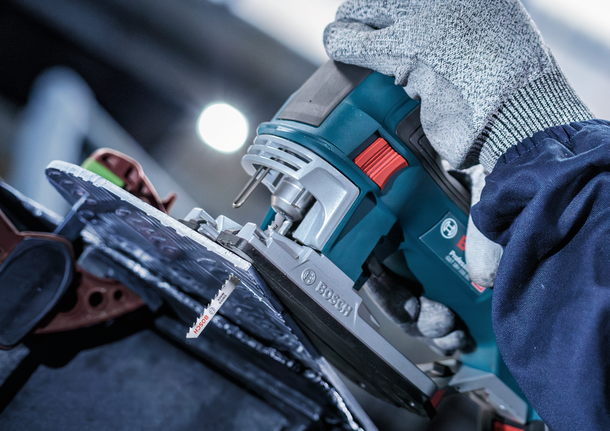 บุคคลที่สวมอุปกรณ์ความปลอดภัยใช้จิ๊กซอว์ตัดผ่านแผ่นวัสดุ