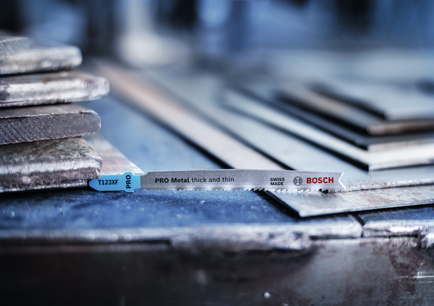 ใบเลื่อยจิ๊กซอว์วางอยู่บนแผ่นโลหะที่วางซ้อนกันในโรงงาน