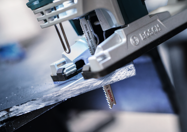 จิ๊กซอว์กำลังตัดแผ่นโลหะสีเข้มในโรงงานแห่งหนึ่ง