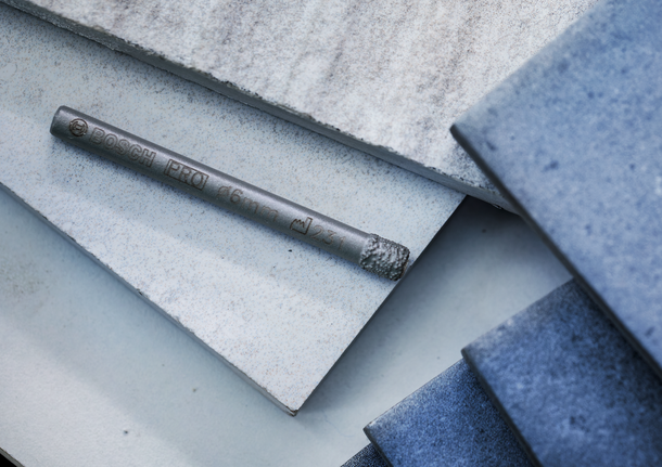 ดอกสว่านสำหรับปูกระเบื้องวางอยู่บนกระเบื้องเซรามิกและกระเบื้องสีฟ้าที่วางซ้อนกัน