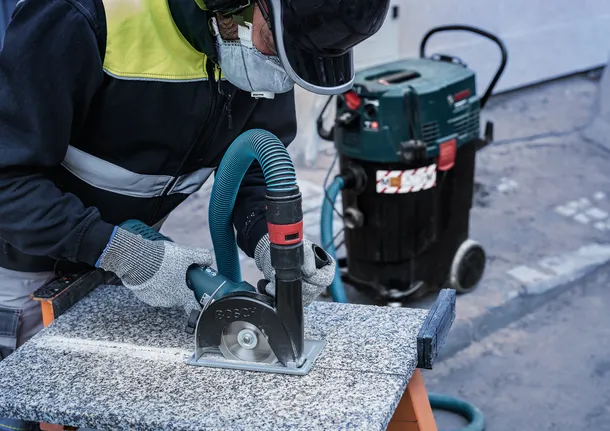 บุคคลที่สวมอุปกรณ์ความปลอดภัยกำลังตัดหินด้วยเลื่อยวงเดือนที่เชื่อมต่อกับเครื่องดูดฝุ่น