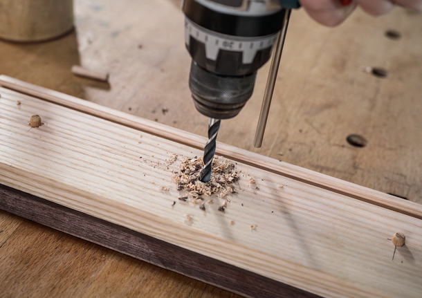 คนกำลังใช้สว่านเจาะรูบนแผ่นไม้