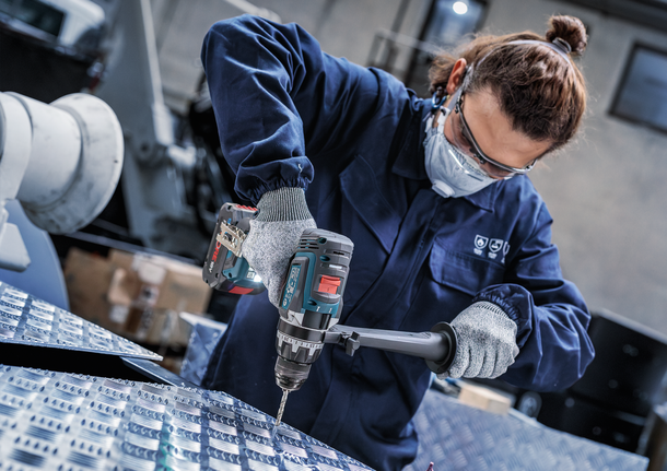 บุคคลที่สวมอุปกรณ์ความปลอดภัยกำลังเจาะเข้าไปในพื้นผิวโลหะ