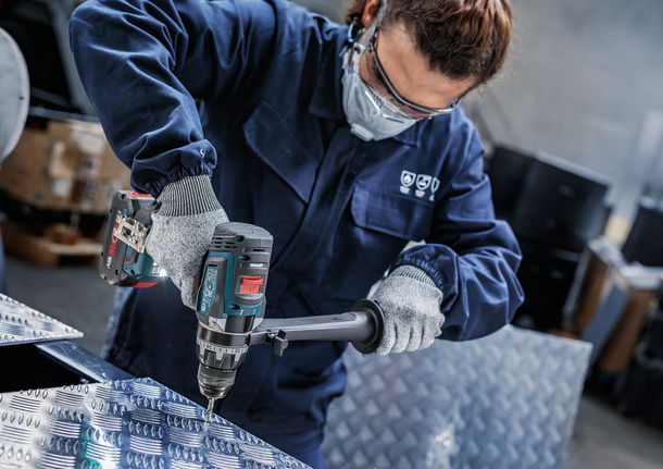 ผู้ที่สวมอุปกรณ์ป้องกันความปลอดภัยกำลังเจาะแผ่นโลหะ