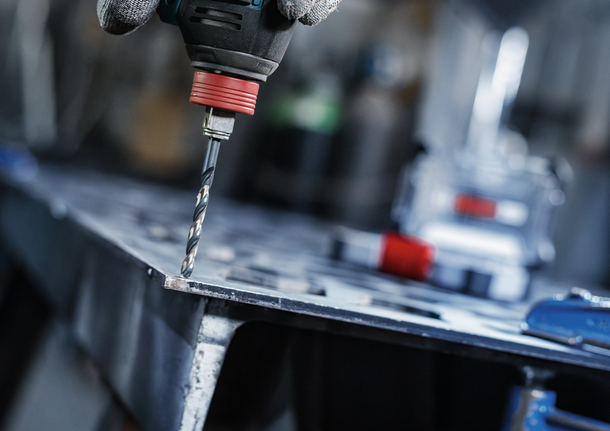 บุคคลที่สวมอุปกรณ์ความปลอดภัยกำลังเจาะรูบนแผ่นโลหะ