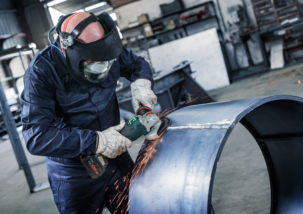 บุคคลที่สวมอุปกรณ์ความปลอดภัยบดขอบท่อโลหะขนาดใหญ่ ทำให้เกิดประกายไฟ