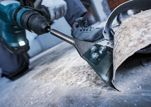 ผู้ที่สวมอุปกรณ์ด้านความปลอดภัยกำลังถอดวัสดุพื้นออกโดยใช้สิ่วไฟฟ้า