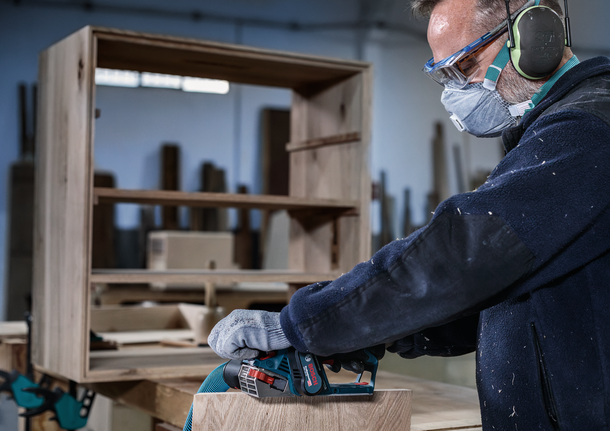 บุคคลที่สวมอุปกรณ์ความปลอดภัยขัดเฟอร์นิเจอร์ไม้ด้วยเครื่องมือไฟฟ้า