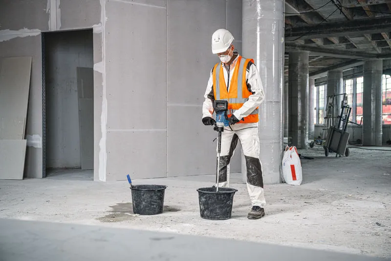 บุคคลที่สวมอุปกรณ์ด้านความปลอดภัยใช้กลไกการกวนเพื่อผสมวัสดุในถัง.