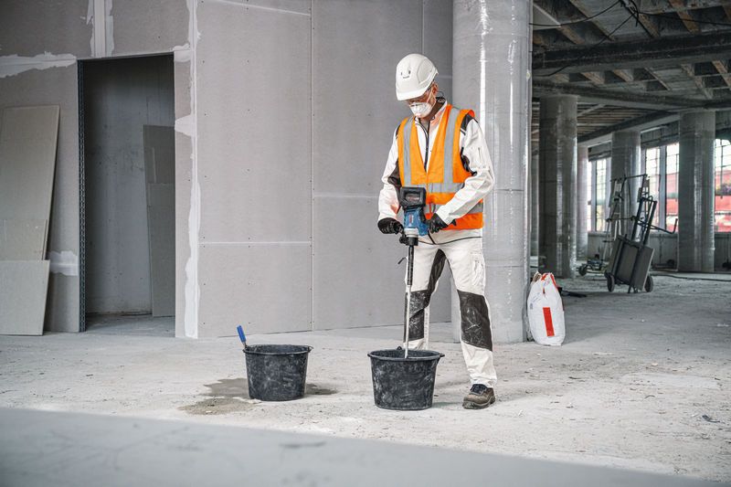 บุคคลที่สวมอุปกรณ์ด้านความปลอดภัยใช้กลไกการกวนเพื่อผสมวัสดุในถัง.