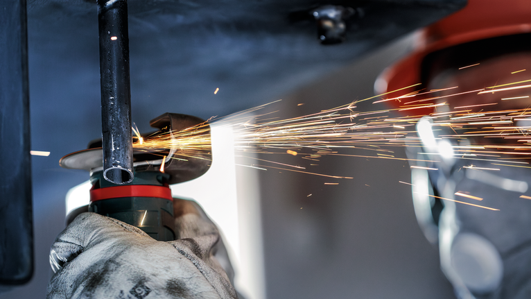 บุคคลที่สวมอุปกรณ์ความปลอดภัยบดท่อโลหะขณะมีประกายไฟพุ่งออกมา.