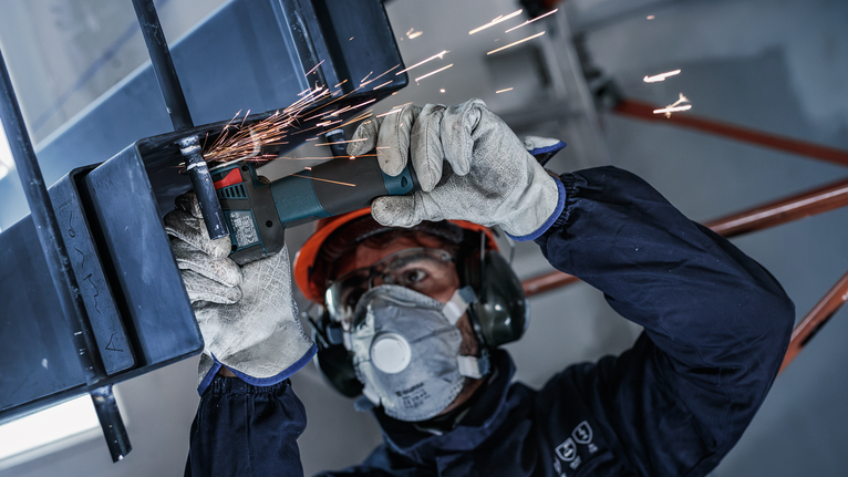 บุคคลที่สวมอุปกรณ์ความปลอดภัยทำการเจียรโลหะ ทำให้เกิดประกายไฟ