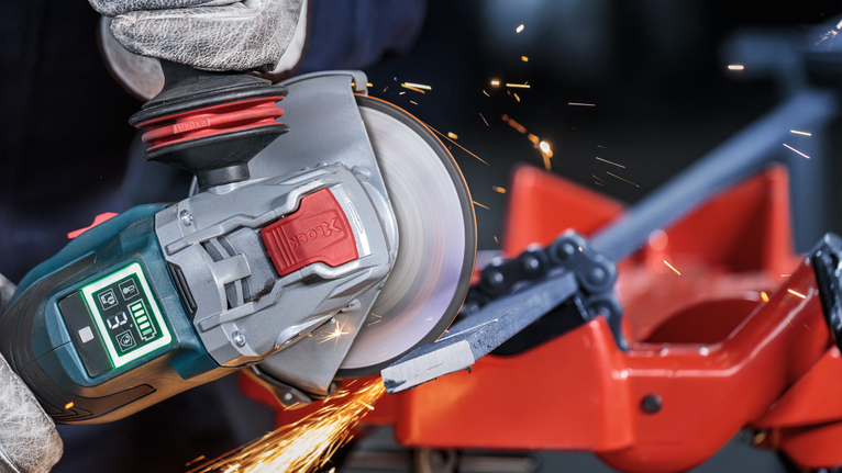 บุคคลที่สวมอุปกรณ์ความปลอดภัยใช้เครื่องเจียรตัดแท่งโลหะ