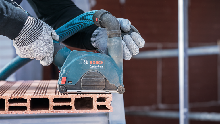 บุคคลที่สวมอุปกรณ์ด้านความปลอดภัยกำลังขัดบล็อกอิฐด้วยเครื่องมือไฟฟ้า