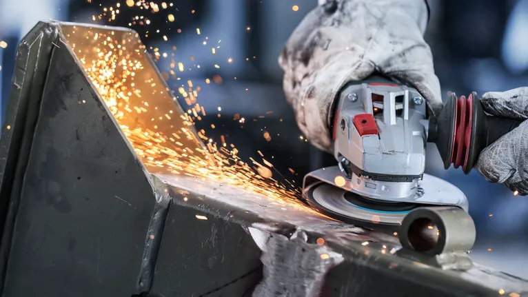 บุคคลที่สวมอุปกรณ์ความปลอดภัยกำลังเจียรโลหะด้วยเครื่องเจียรทำให้เกิดประกายไฟ