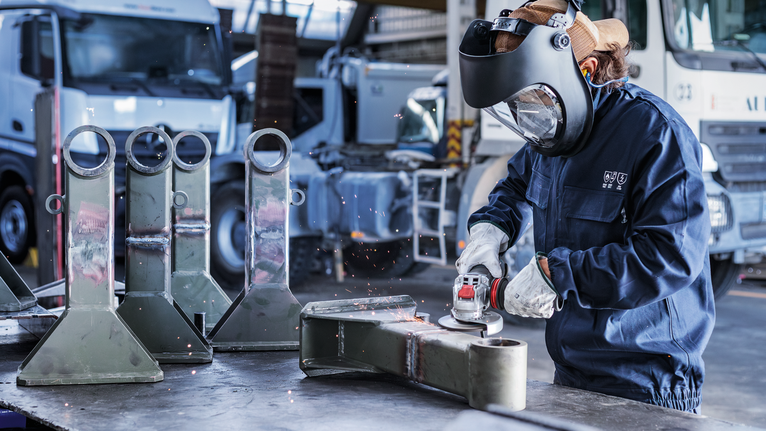 บุคคลที่สวมอุปกรณ์ความปลอดภัยกำลังเจียรชิ้นส่วนโลหะในสถานประกอบการอุตสาหกรรม