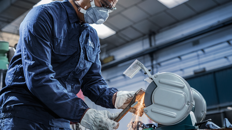 บุคคลที่สวมอุปกรณ์ความปลอดภัยใช้เลื่อยตัดโลหะตัดท่อ ทำให้เกิดประกายไฟ