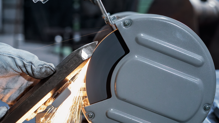 บุคคลที่สวมอุปกรณ์ความปลอดภัยกำลังเจียรแท่งโลหะด้วยเครื่องเจียรแท่น