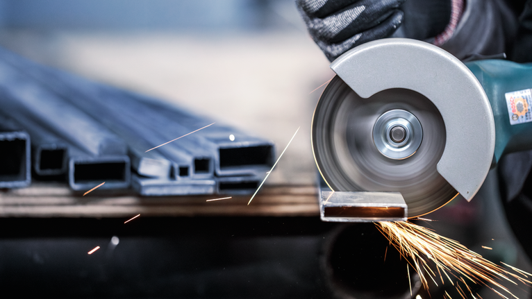 ผู้ที่สวมอุปกรณ์ป้องกันความปลอดภัยตัดท่อโลหะด้วยเลื่อยวงเดือน ทำให้มีประกายไฟกระเด็นออกมา