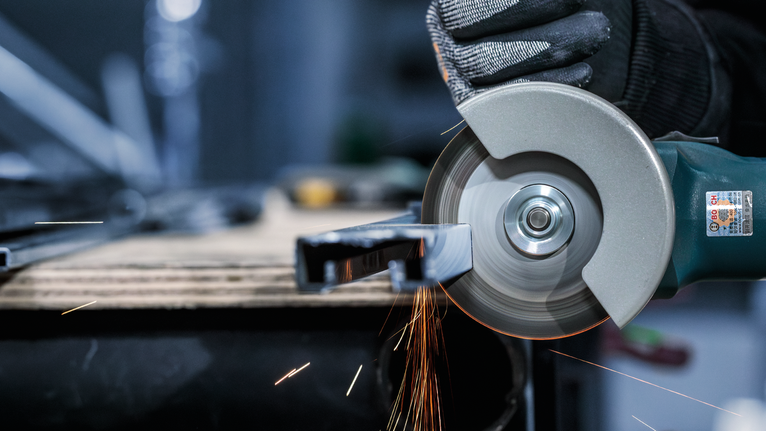 บุคคลที่สวมอุปกรณ์ความปลอดภัยใช้เครื่องเจียรตัดโลหะ ทำให้เกิดประกายไฟ