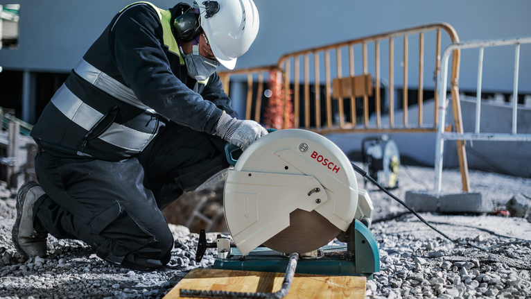 คนงานสวมอุปกรณ์ความปลอดภัยกำลังตัดเหล็กเส้นด้วยเลื่อยตัดที่ไซต์ก่อสร้าง.