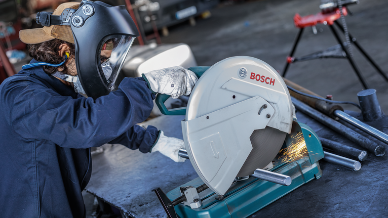 ผู้ที่สวมอุปกรณ์ป้องกันความปลอดภัยตัดท่อโลหะด้วยเลื่อยวงเดือน มีประกายไฟกระเด็นออกมา.