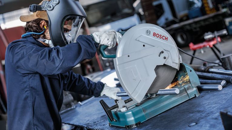 บุคคลที่สวมอุปกรณ์ความปลอดภัยตัดท่อโลหะด้วยเลื่อยไฟฟ้า ทำให้เกิดประกายไฟ