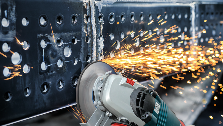 เครื่องเจียรไฟฟ้ากำลังตัดผ่านคานโลหะในขณะที่มีประกายไฟพุ่งออกมา.