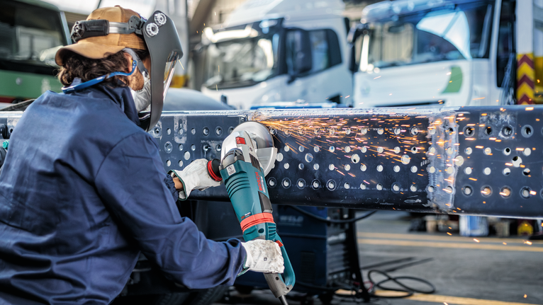 บุคคลที่สวมอุปกรณ์ป้องกันความปลอดภัยทำการบดคานโลหะทำให้เกิดประกายไฟ.