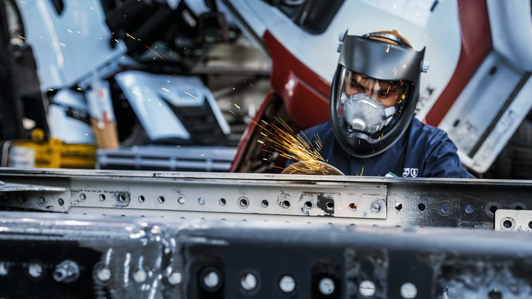 บุคคลที่สวมอุปกรณ์ป้องกันความปลอดภัยทำการบดโลหะ ทำให้เกิดประกายไฟสว่าง.