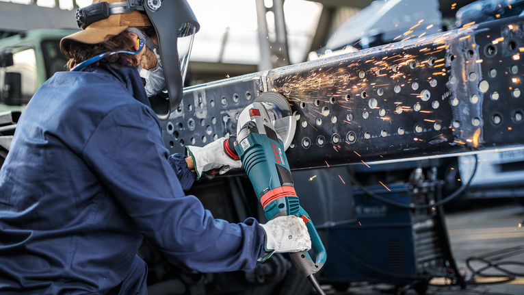 บุคคลที่สวมอุปกรณ์ป้องกันความปลอดภัยกำลังบดลำแสงโลหะ ทำให้เกิดประกายไฟสว่าง.