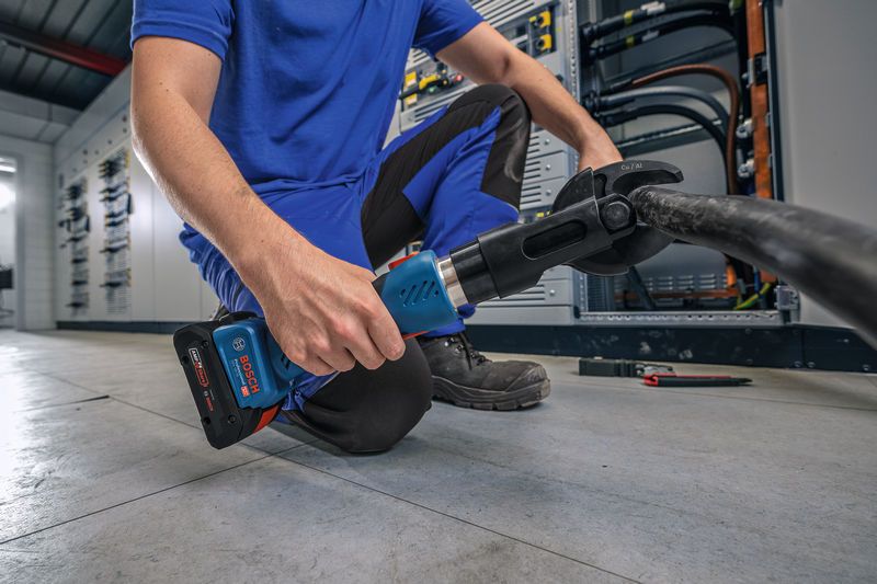 บุคคลที่สวมอุปกรณ์ด้านความปลอดภัยใช้เครื่องมือตัดไฮดรอลิกแบบไร้สายบนสายเคเบิลหนา.