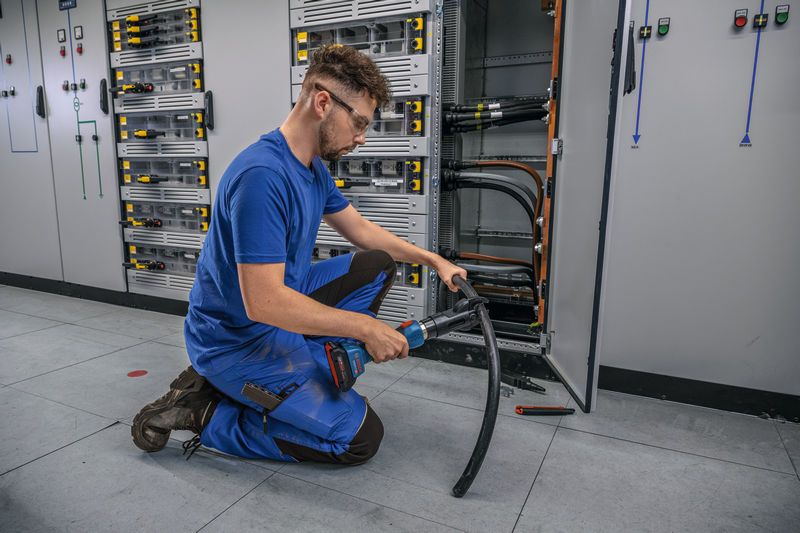 บุคคลที่สวมอุปกรณ์ด้านความปลอดภัยใช้เครื่องมือตัดไฮดรอลิกแบบไร้สายบนสายเคเบิลหนา.