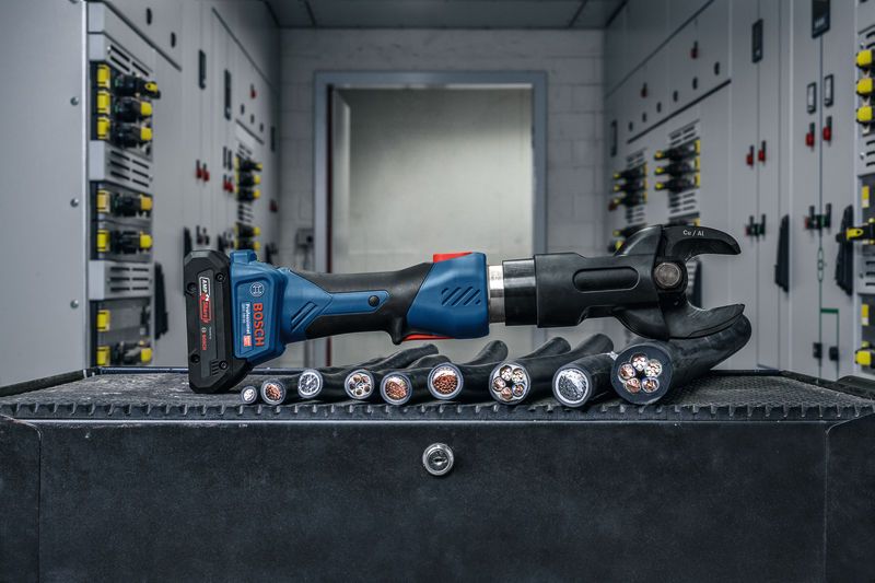 เครื่องมือตัดไฮดรอลิกแบบไร้สายวางอยู่บนโต๊ะทำงานข้างสายไฟหนา.