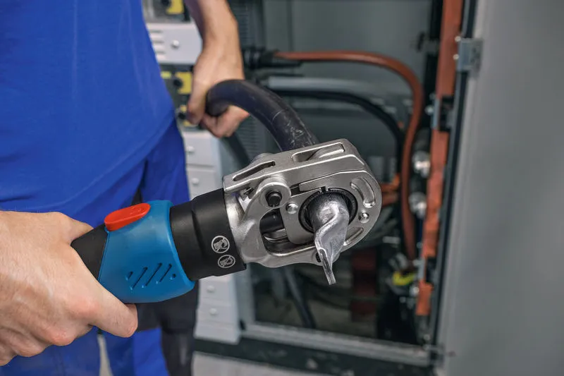 คนใช้เครื่องมือจีบไฮดรอลิกแบบไร้สายกับสายเคเบิลหนาใกล้แผงไฟฟ้า.