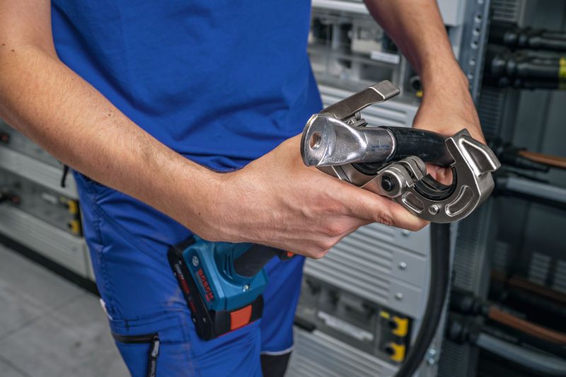 บุคคลที่สวมอุปกรณ์ด้านความปลอดภัยใช้เครื่องมือจีบไฮดรอลิกแบบไร้สายกับสายเคเบิล.