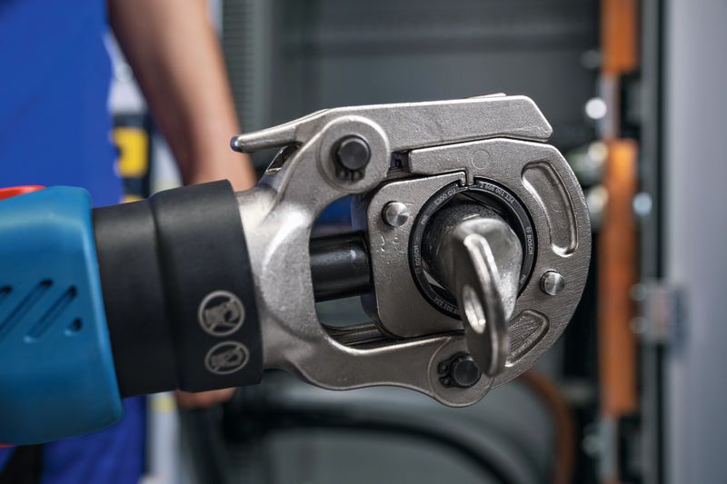 บุคคลที่สวมอุปกรณ์ด้านความปลอดภัยกำลังใช้งานเครื่องมือจีบไฮดรอลิกแบบไร้สายหน้าแผง.