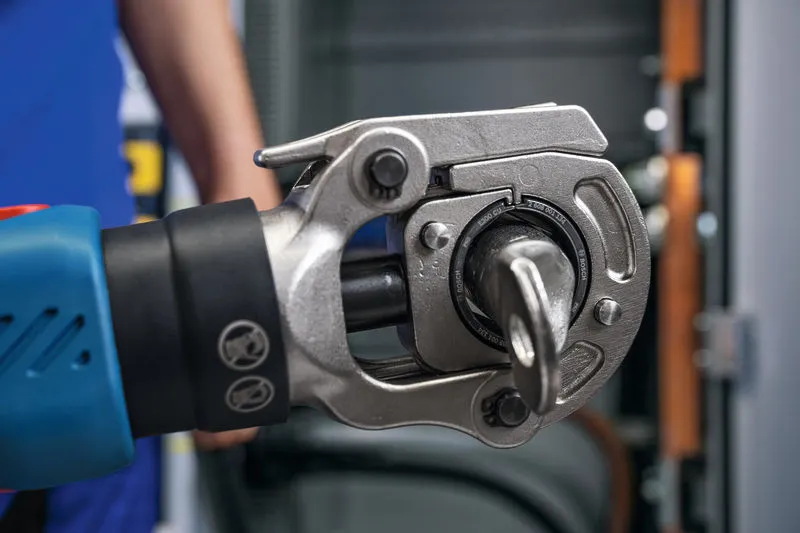 บุคคลที่สวมอุปกรณ์ด้านความปลอดภัยกำลังใช้งานเครื่องมือจีบไฮดรอลิกแบบไร้สายหน้าแผง.