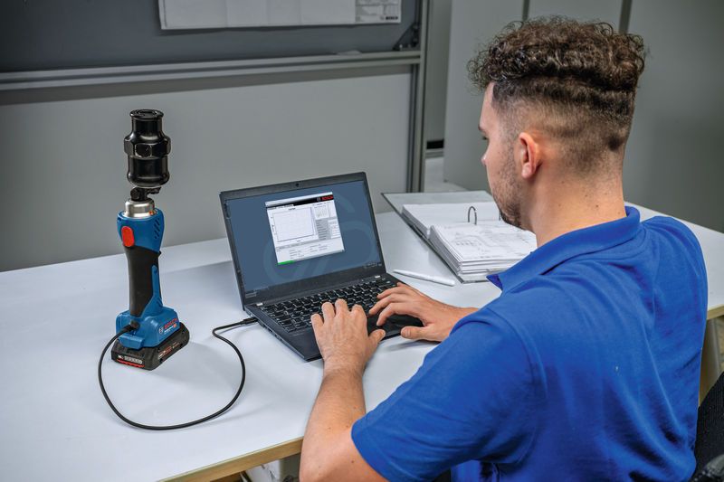 คนๆ หนึ่งกำลังเชื่อมต่อเครื่องเจาะไฮดรอลิกแบบไร้สายเข้ากับแล็ปท็อปที่โต๊ะ.