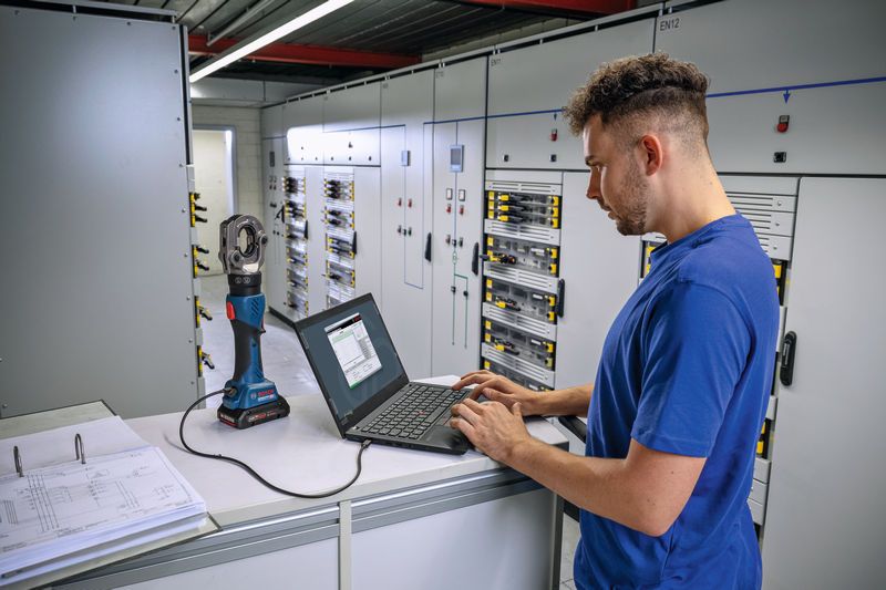 บุคคลดังกล่าวกำลังใช้งานแล็ปท็อปที่เชื่อมต่อกับเครื่องมือจีบไฮดรอลิกแบบไร้สายในห้องควบคุมไฟฟ้า.