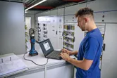 บุคคลดังกล่าวกำลังใช้งานแล็ปท็อปที่เชื่อมต่อกับเครื่องมือจีบไฮดรอลิกแบบไร้สายในห้องควบคุมไฟฟ้า.