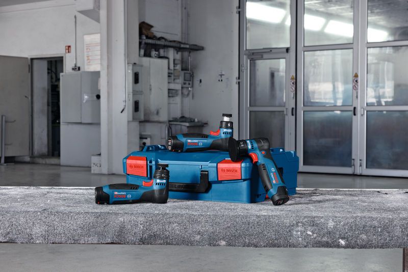 เครื่องขัดสุ่มวงโคจรแบบไร้สายและเคสสีน้ำเงินวางอยู่บนพื้นคอนกรีตในโรงงาน.