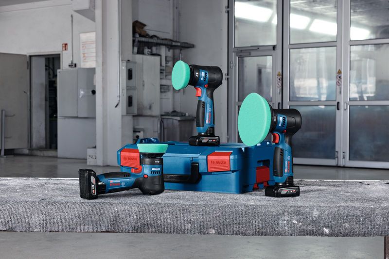 เครื่องขัดแบบไร้สายจำนวน 3 เครื่อง พร้อมแผ่นขัดสีเขียว วางอยู่บนเคสสีน้ำเงินในโรงงานแห่งหนึ่ง.