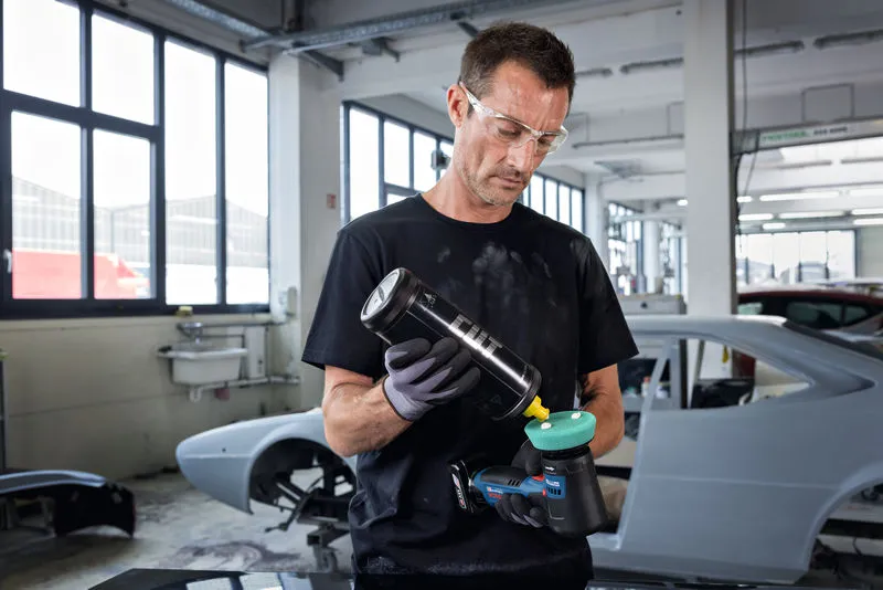 บุคคลที่สวมอุปกรณ์ด้านความปลอดภัยกำลังขัดเงาเครื่องขัดไฟฟ้าในอู่ซ่อมรถยนต์.