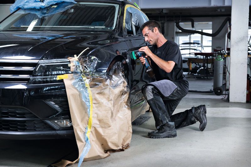 บุคคลที่สวมอุปกรณ์ด้านความปลอดภัยใช้เครื่องขัดเงาบังโคลนรถยนต์ในร้านซ่อมรถยนต์.