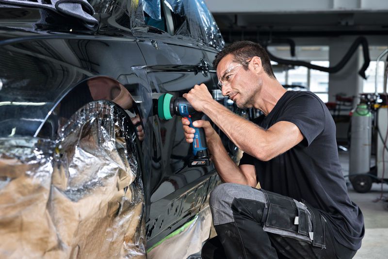 บุคคลที่สวมอุปกรณ์ความปลอดภัยกำลังขัดประตูรถด้วยเครื่องมือไร้สาย.