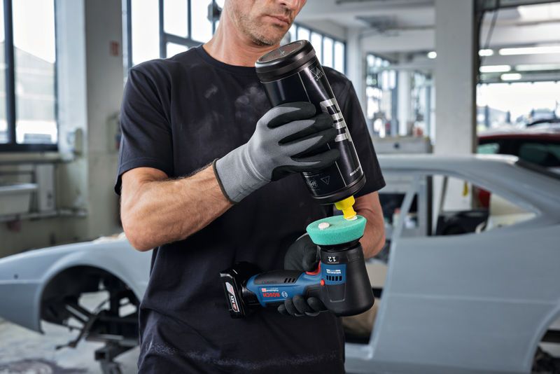 บุคคลที่สวมอุปกรณ์ด้านความปลอดภัยกำลังขัดเงาเครื่องขัดในอู่ซ่อมรถยนต์.